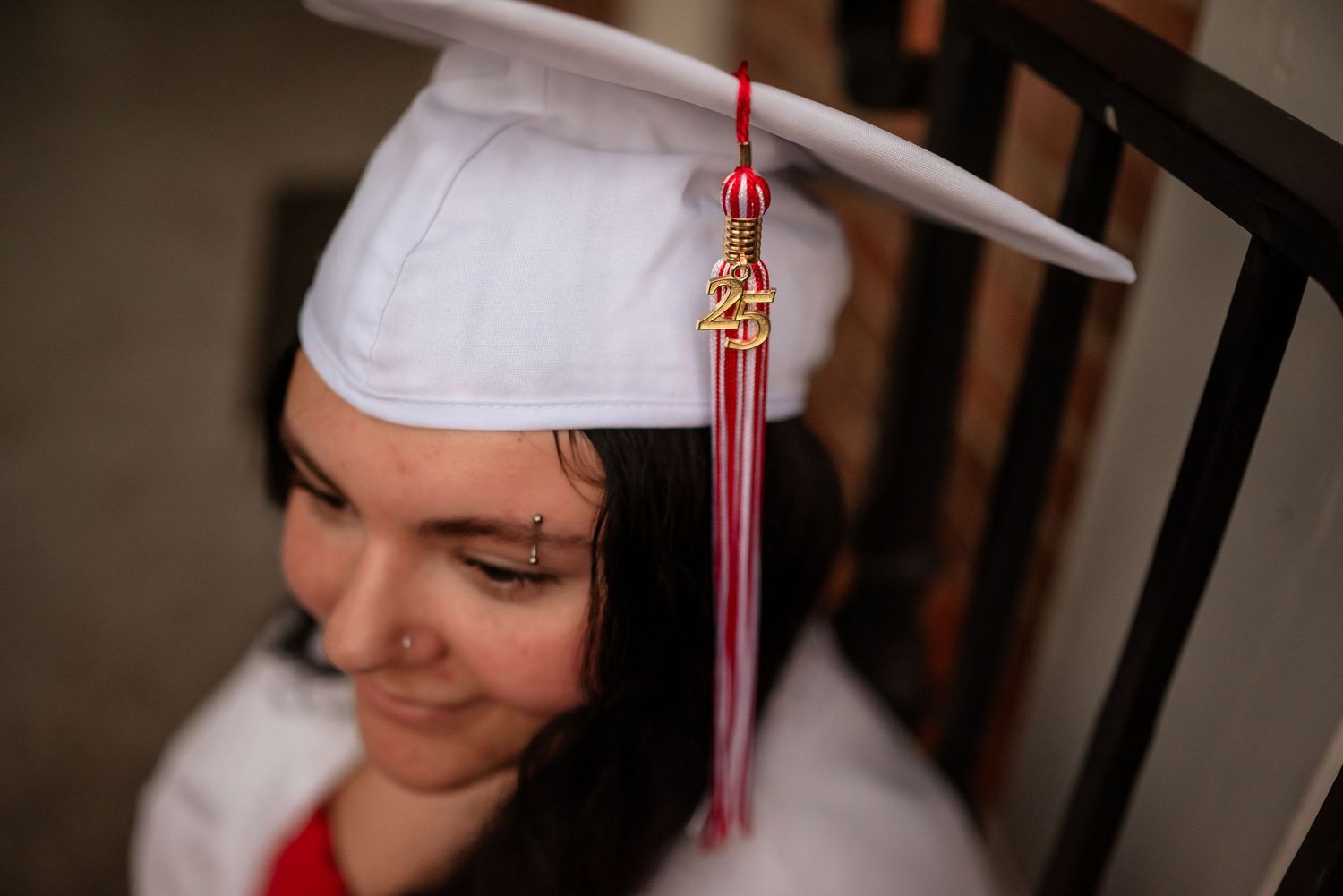 Graduate wearing white cap with red and gold tassel smiles during graduation celebration.