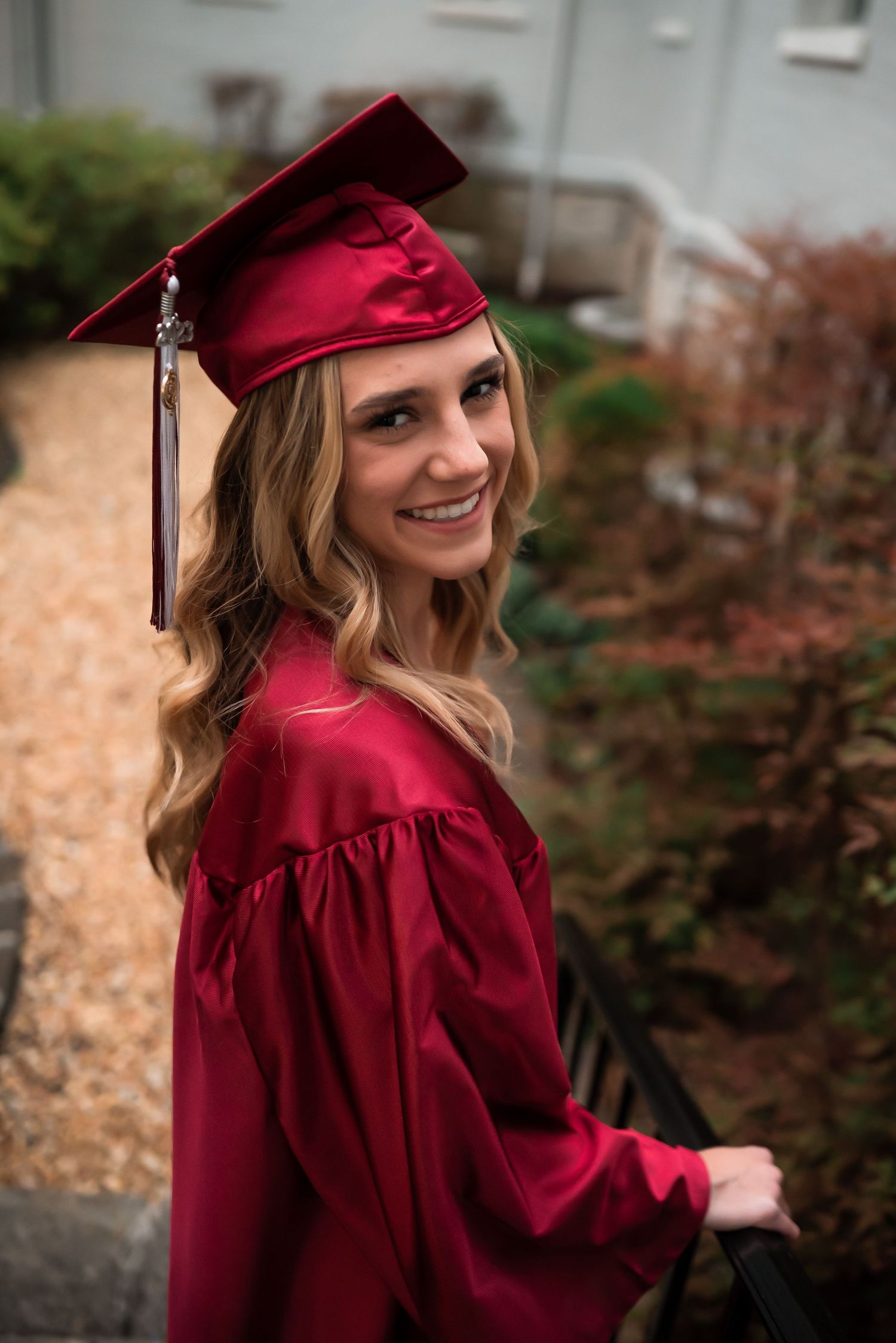 Graduate in red cap and gown poses outdoors during golden hour graduation photoshoot.