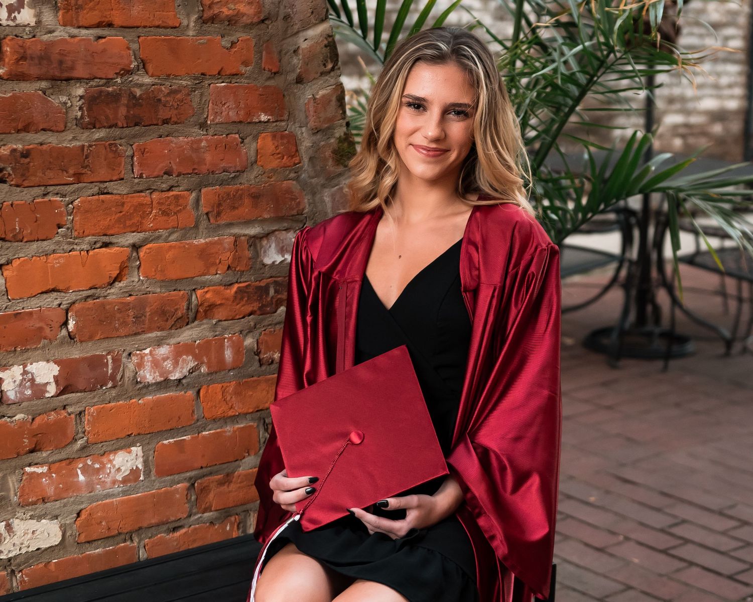 Graduate in red cap and gown poses playfully on stone steps for graduation photos.