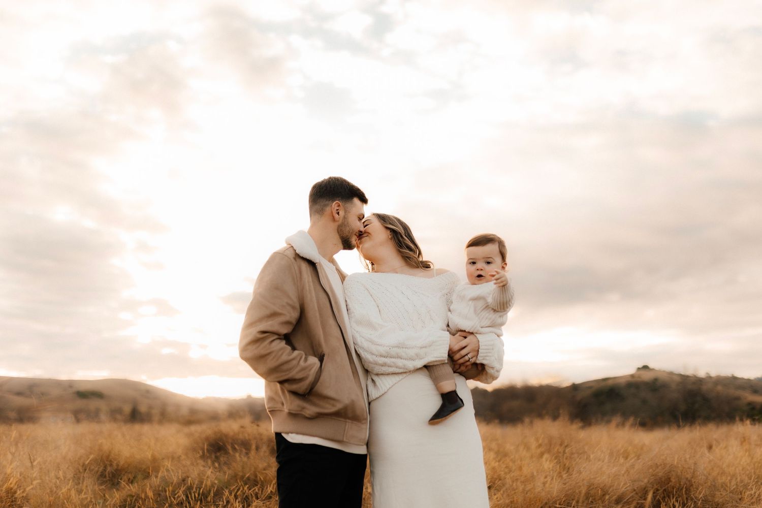Family standing together in golden field at sunset.
