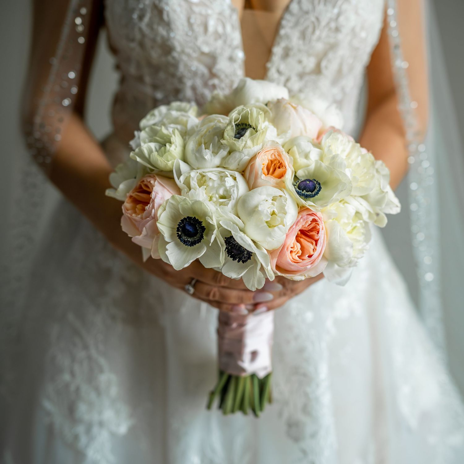 Elegant bridal bouquet featuring white and peach roses with blue accents against a lace wedding gown.