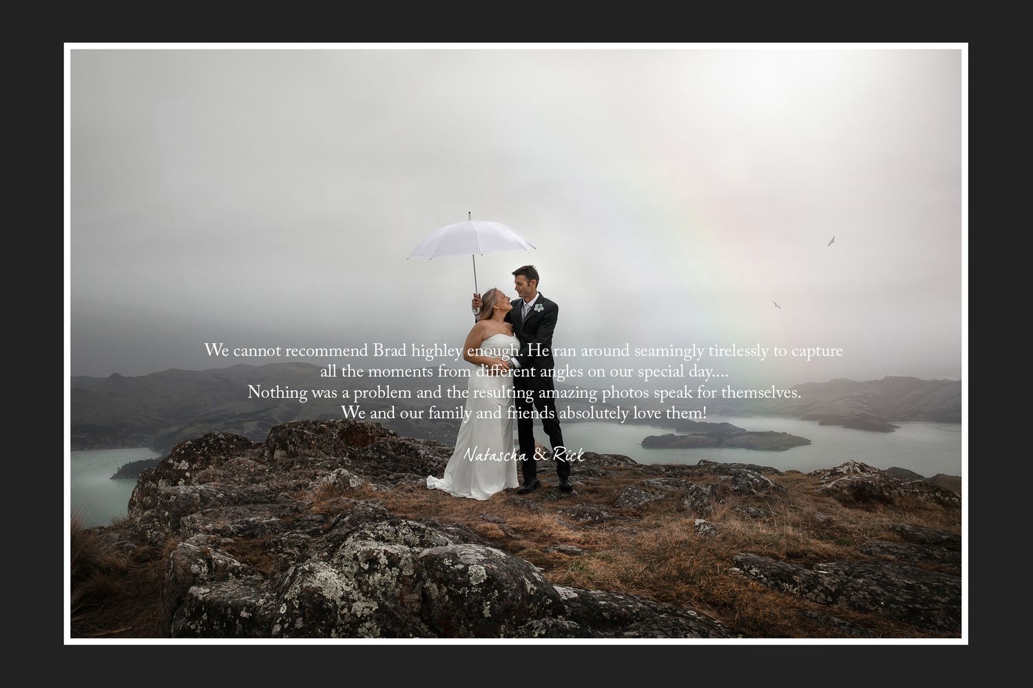 A couple with umbrella stands on cliff edge overlooking misty mountains.