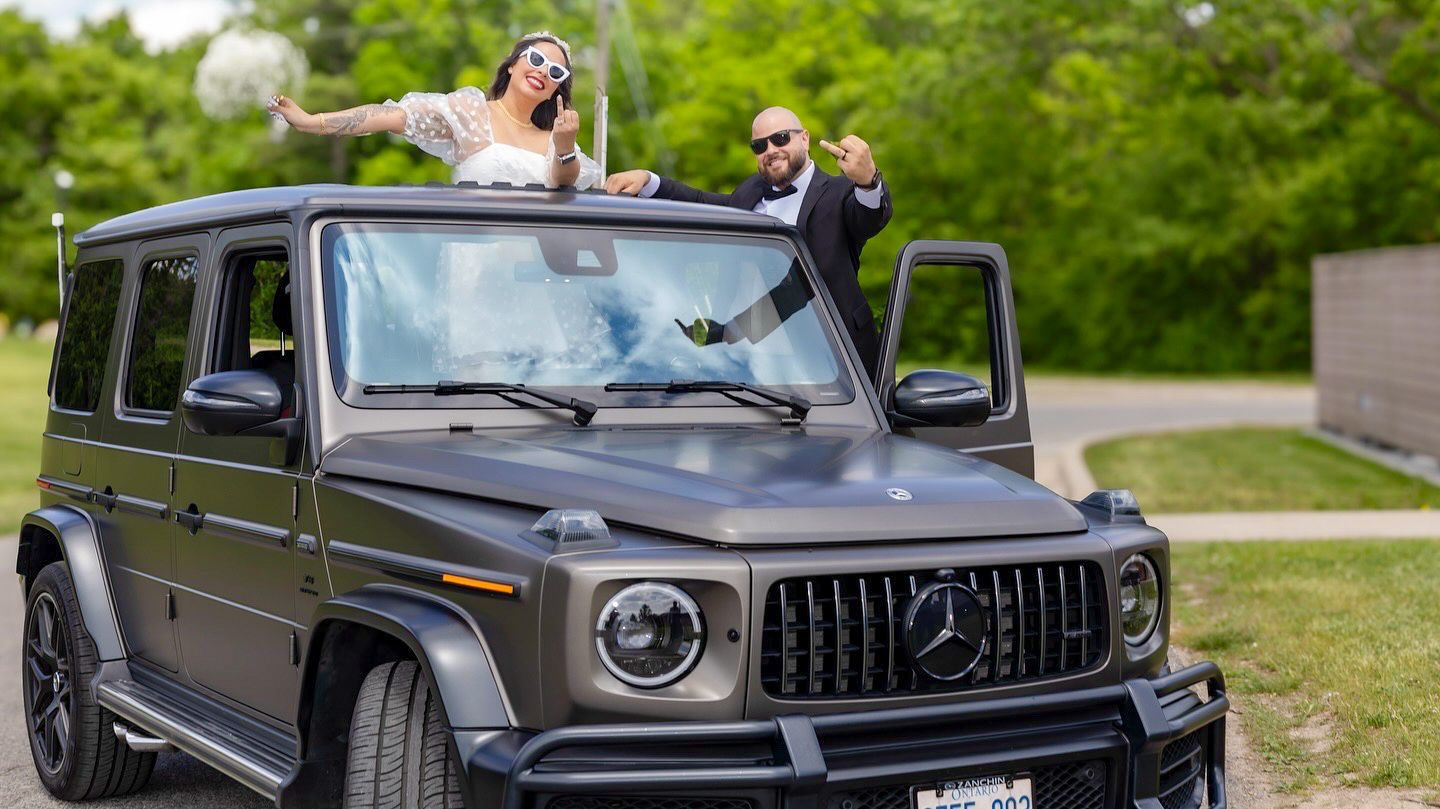 A luxury black Mercedes G-Wagon parked outdoors among green trees.