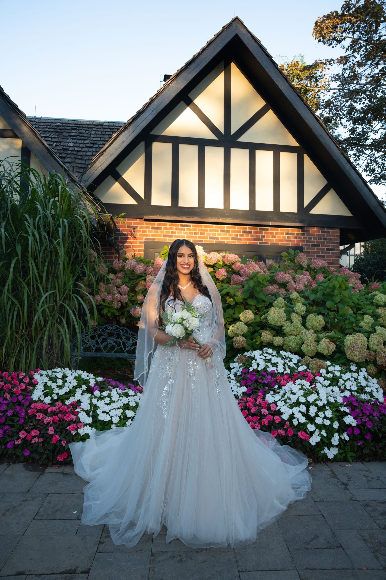 A beautiful wedding scene at dusk with Tudor-style architecture, hydrangeas, and colorful flower beds creating a romantic backdrop.