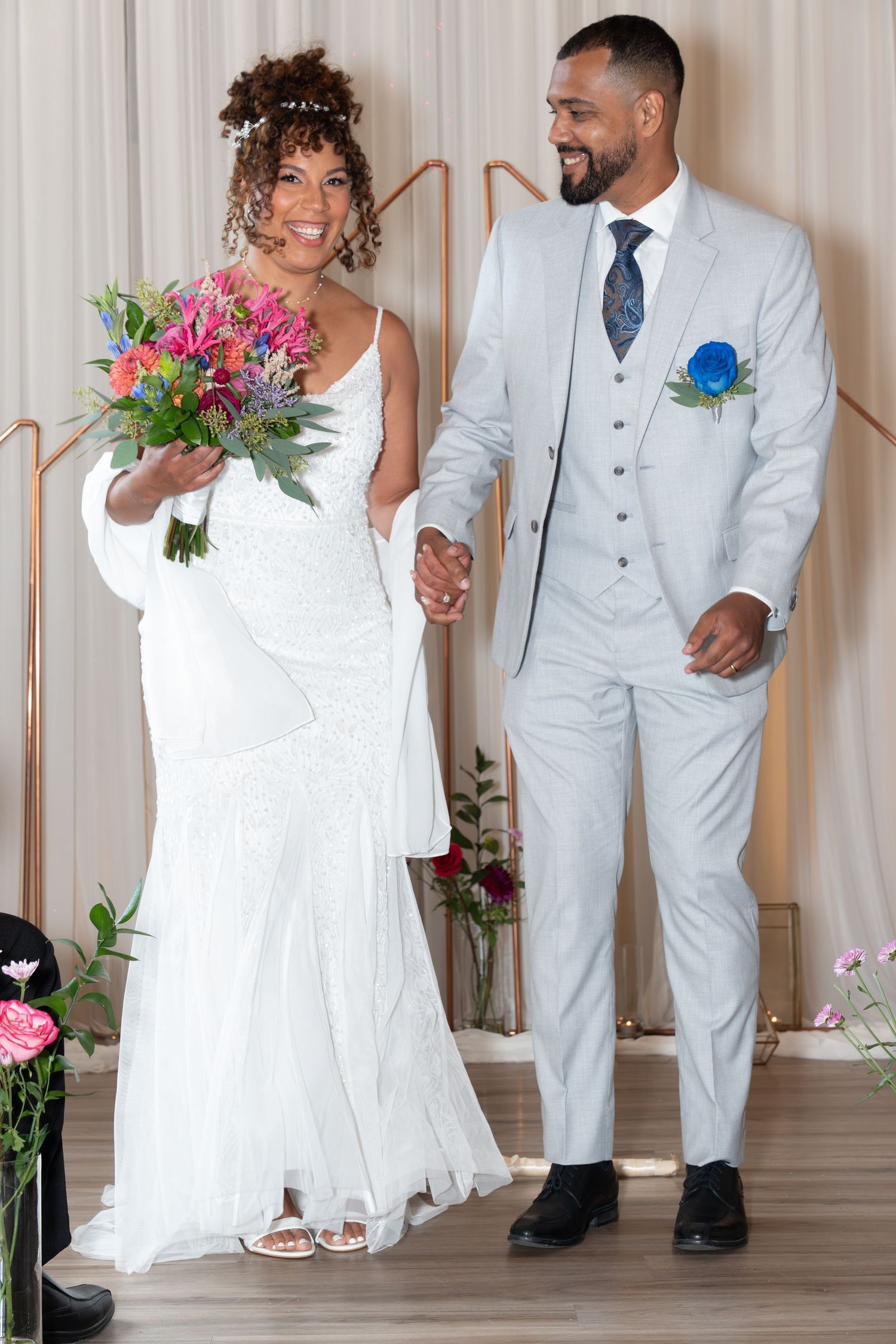 Wedding party in light blue suits and white dresses dancing and celebrating in an elegant indoor venue.