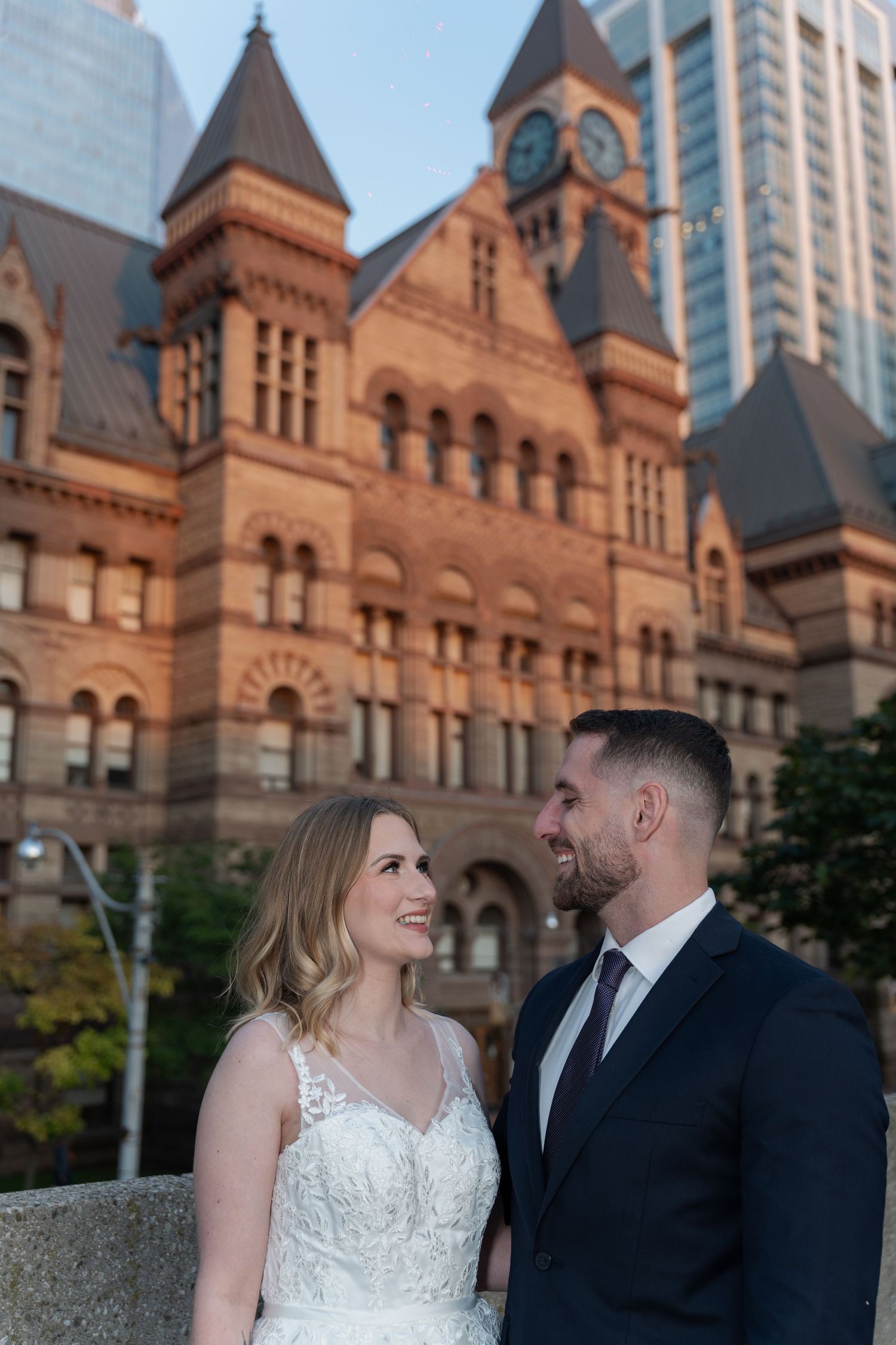 A couple in wedding attire shares romantic moments in front of a historic brick building with arched architecture.