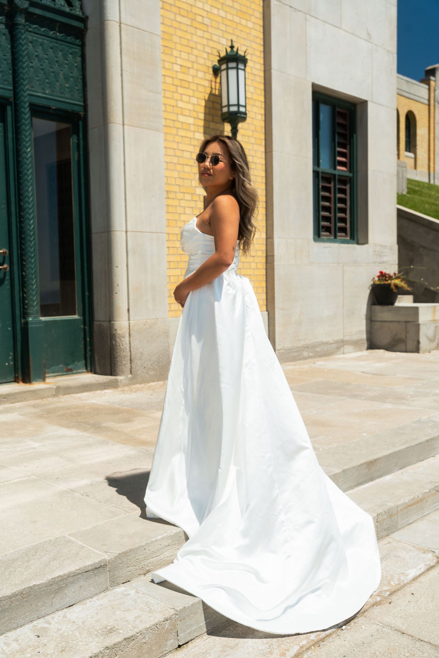 A flowing white wedding dress cascades down stone steps against a yellow building.