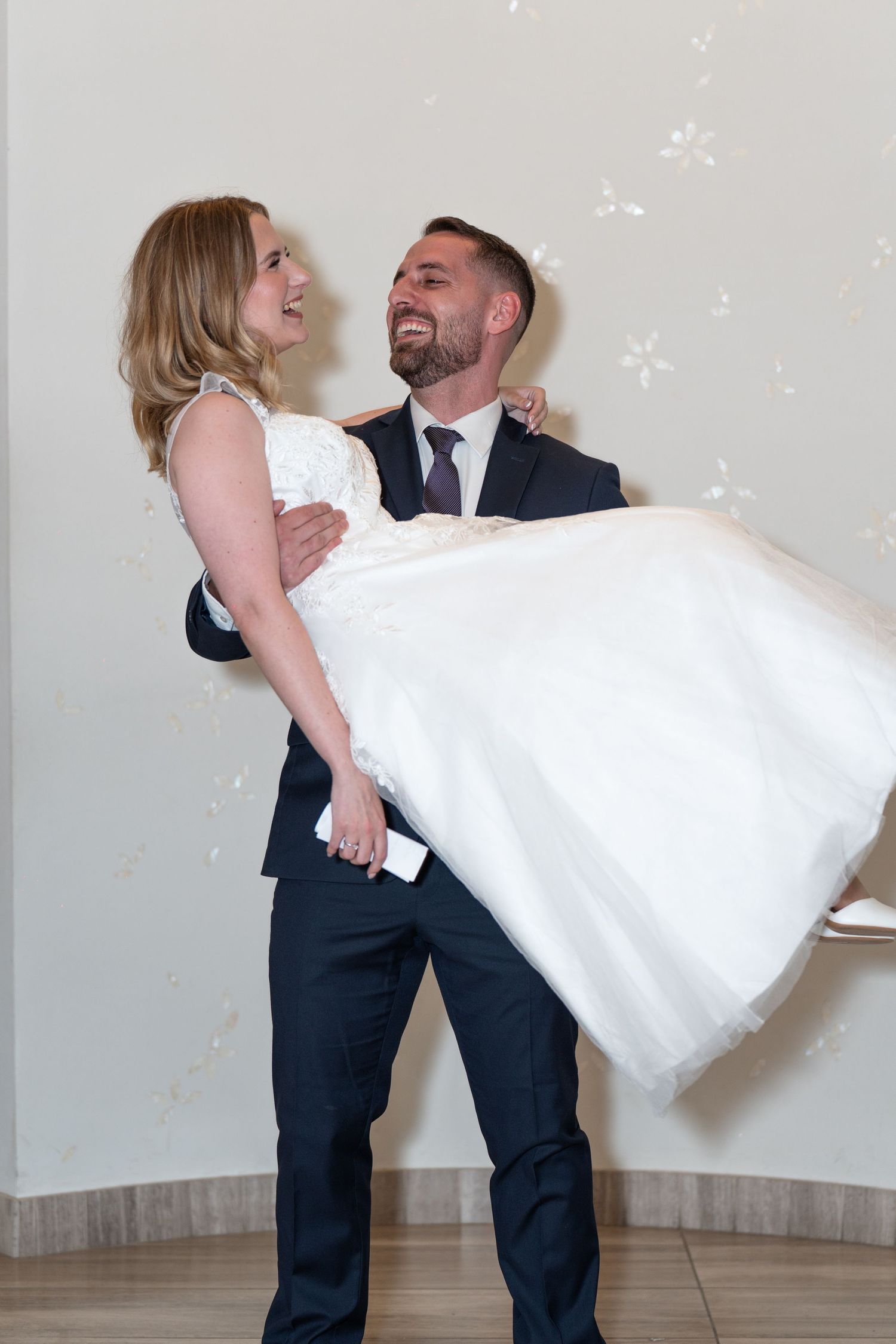 A couple in wedding attire share a romantic dance pose together in a light-filled room.