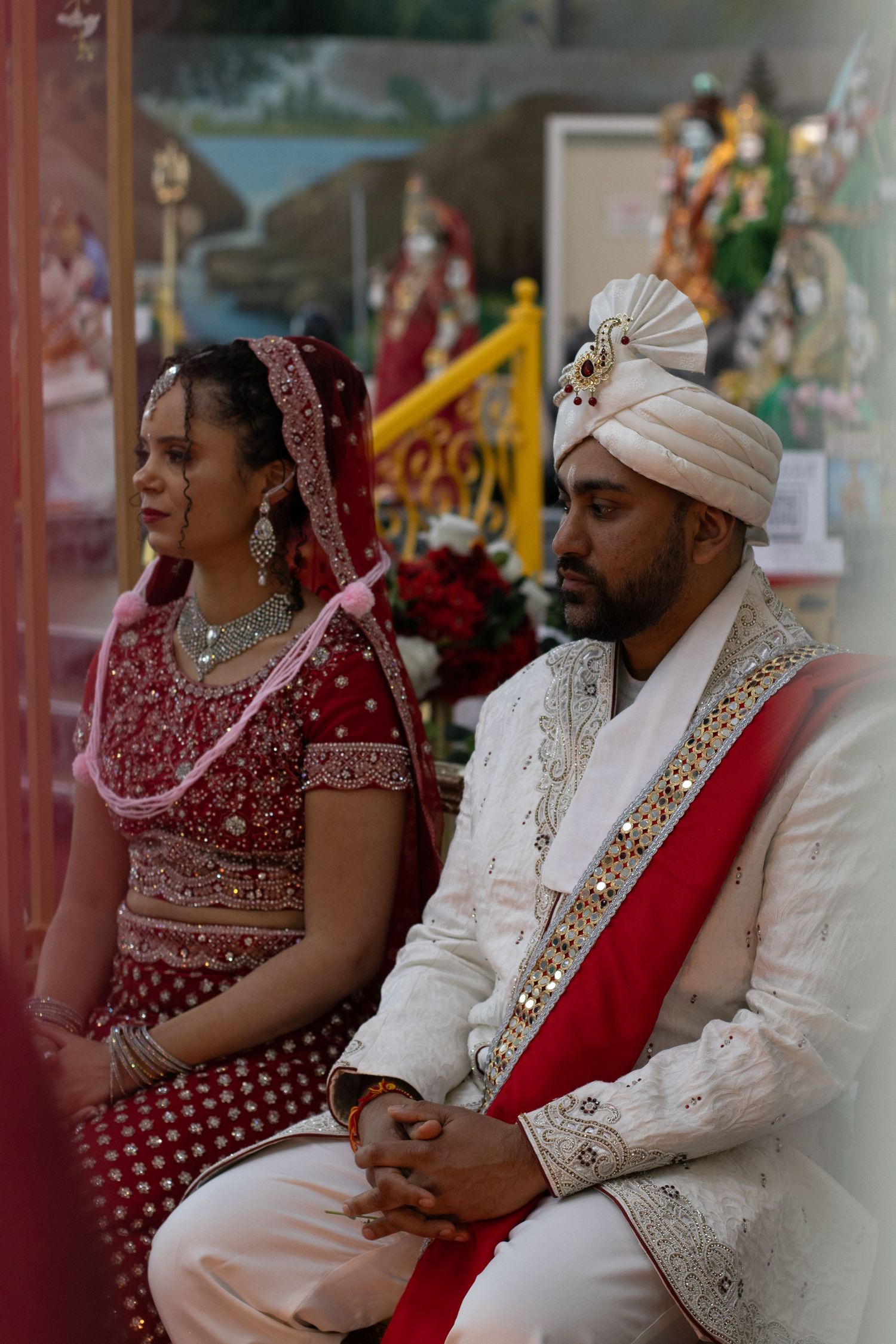 A couple in traditional Indian wedding attire sits together during their ceremony.