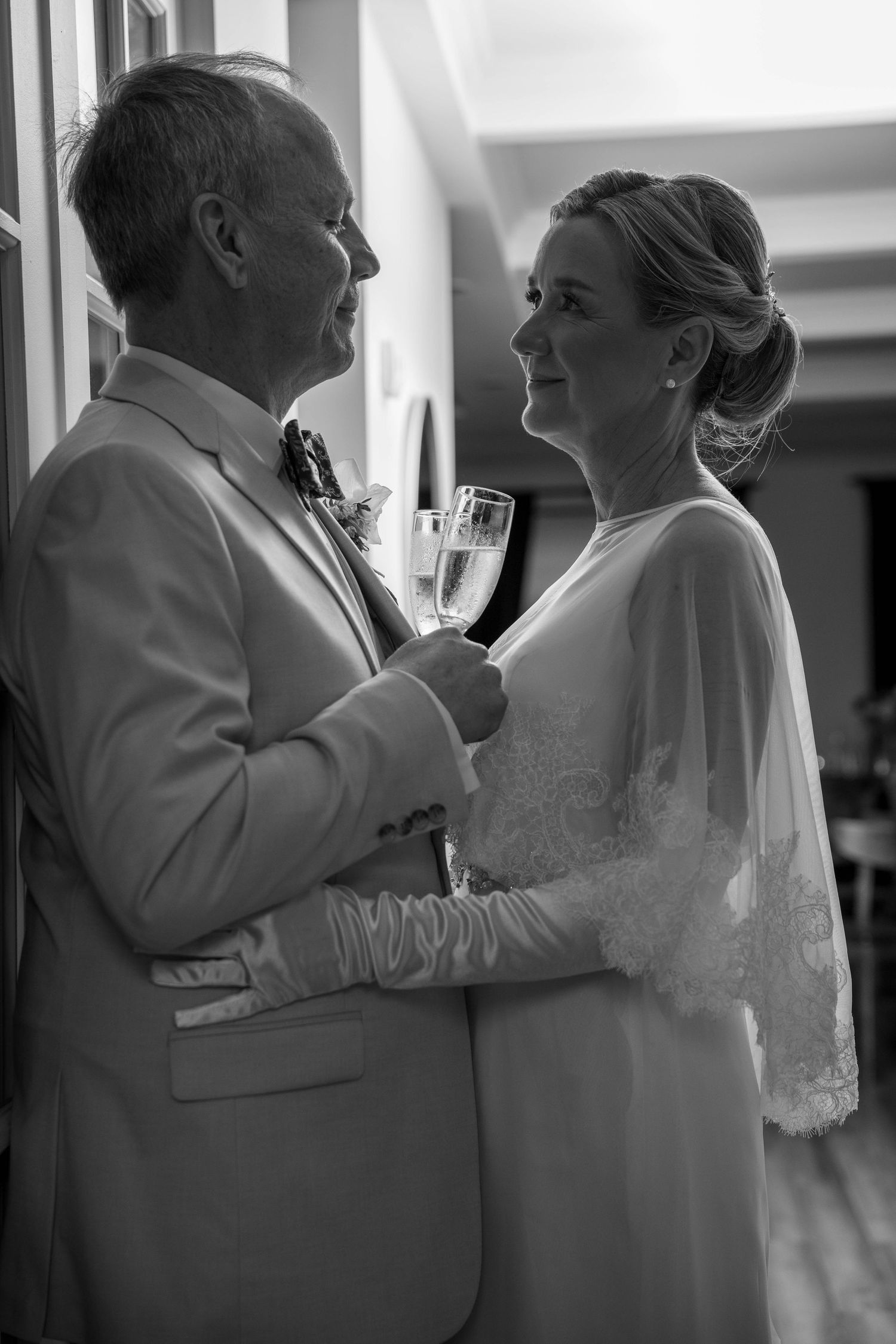 Black and white photo of a bride and groom sharing a champagne toast, gazing lovingly at each other on their wedding day.