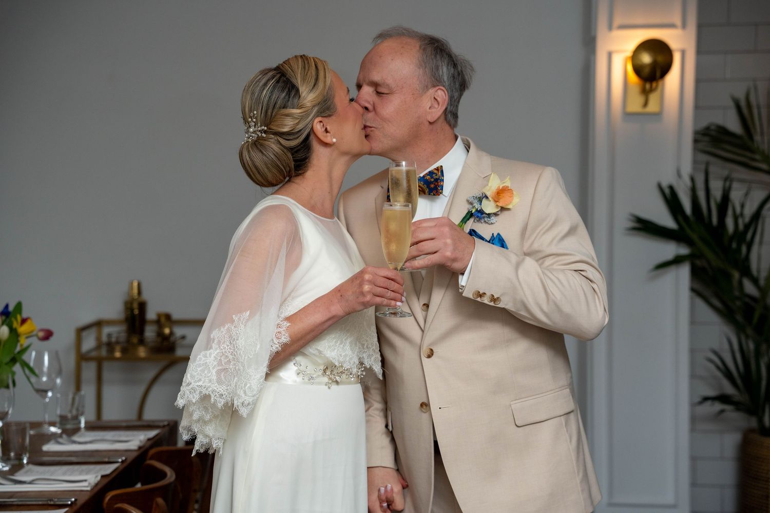 A bride and groom share a kiss while holding champagne glasses during their elegant wedding reception.
