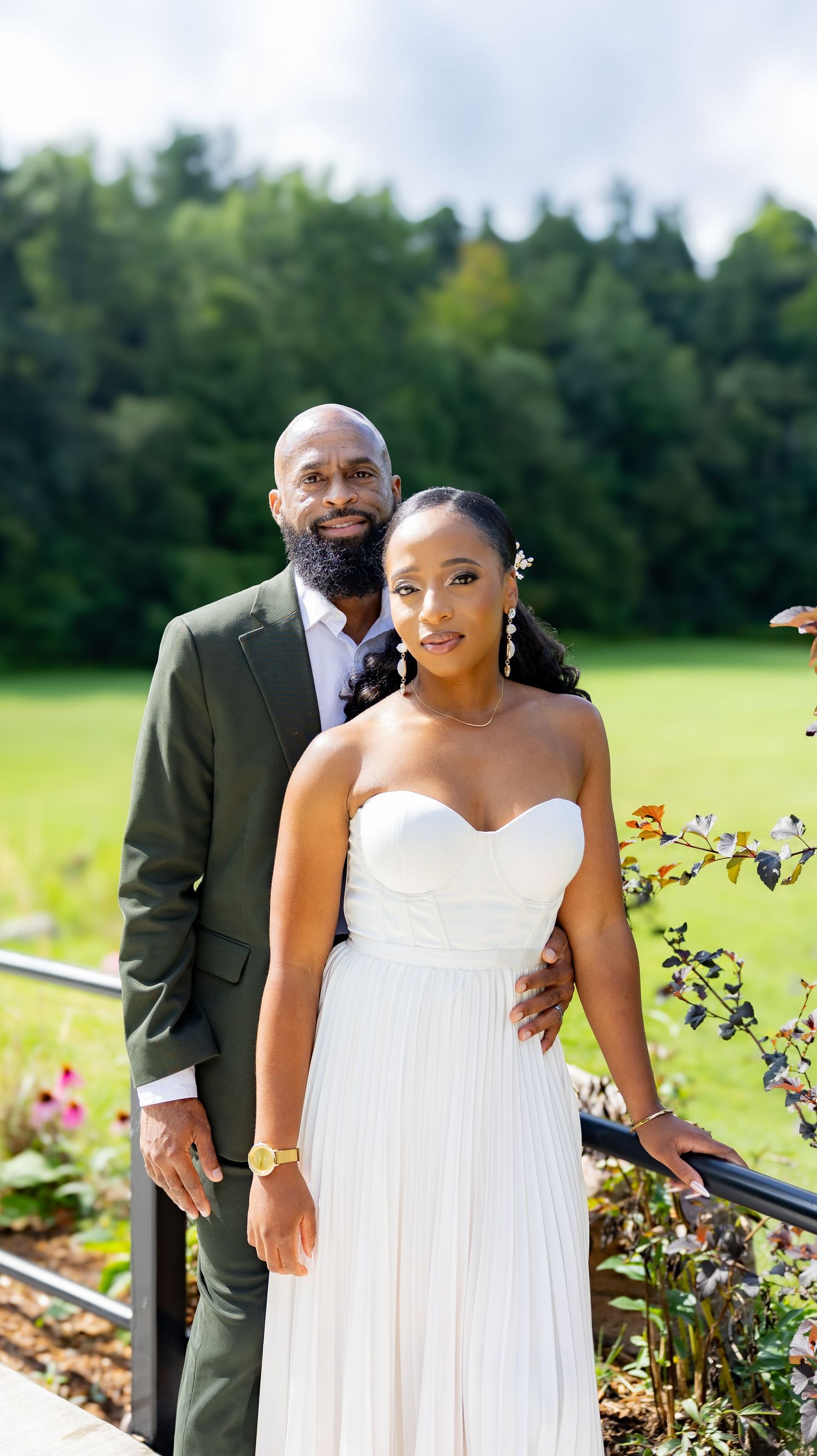 Romantic outdoor wedding photos of couple posing by garden with blooming flowers.