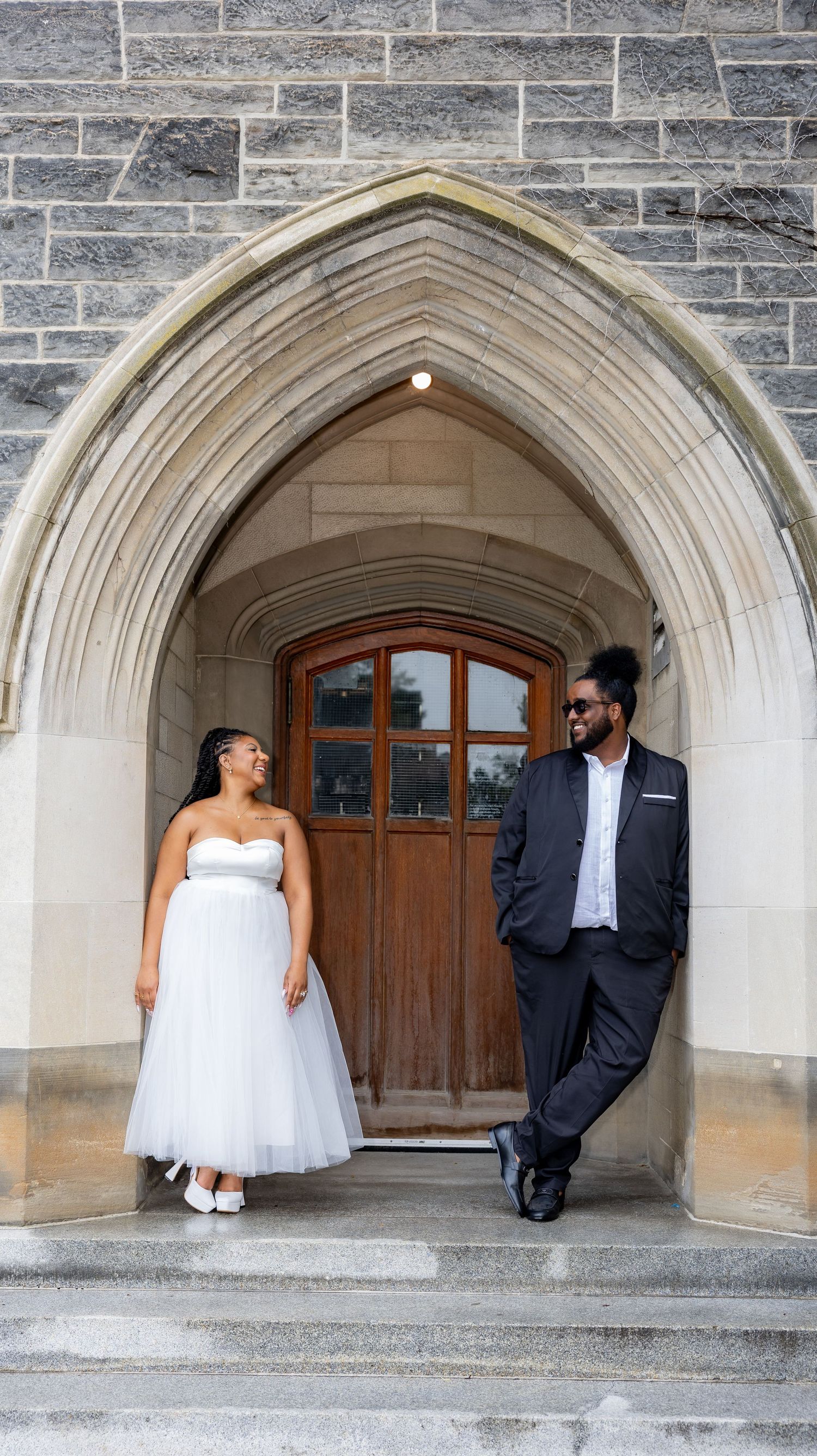 Romantic wedding portraits under stone archway showing couple in formal attire.
