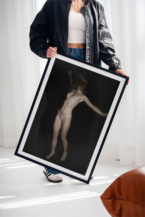 Person in black jacket displaying framed artistic nude photograph against white background.