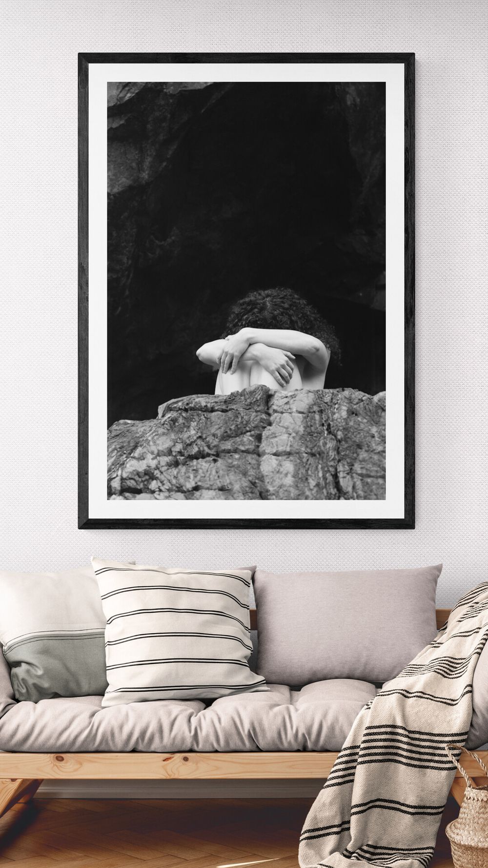 Black and white photograph of abstract art in frames mounted above a modern gray sofa with striped pillows.