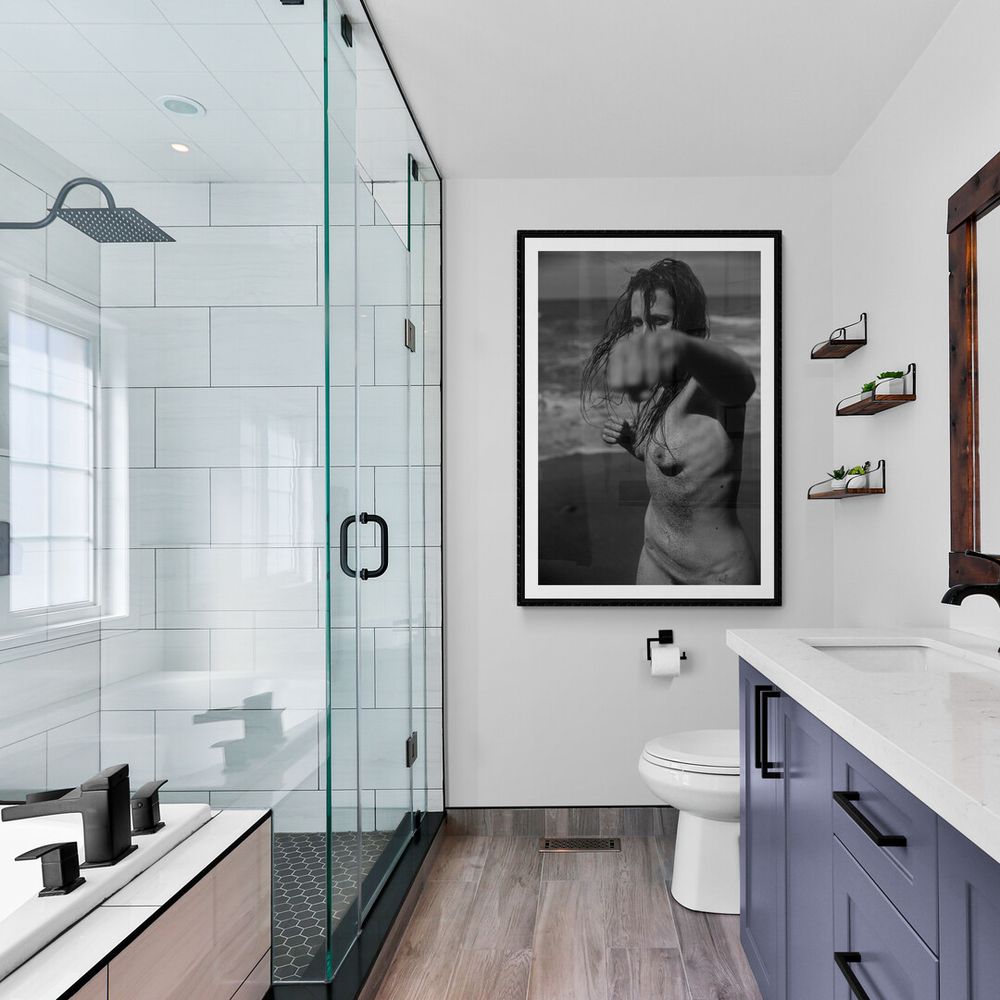 Modern bathroom with glass shower enclosure, navy blue vanity, white marble countertop and dark wood-look flooring.