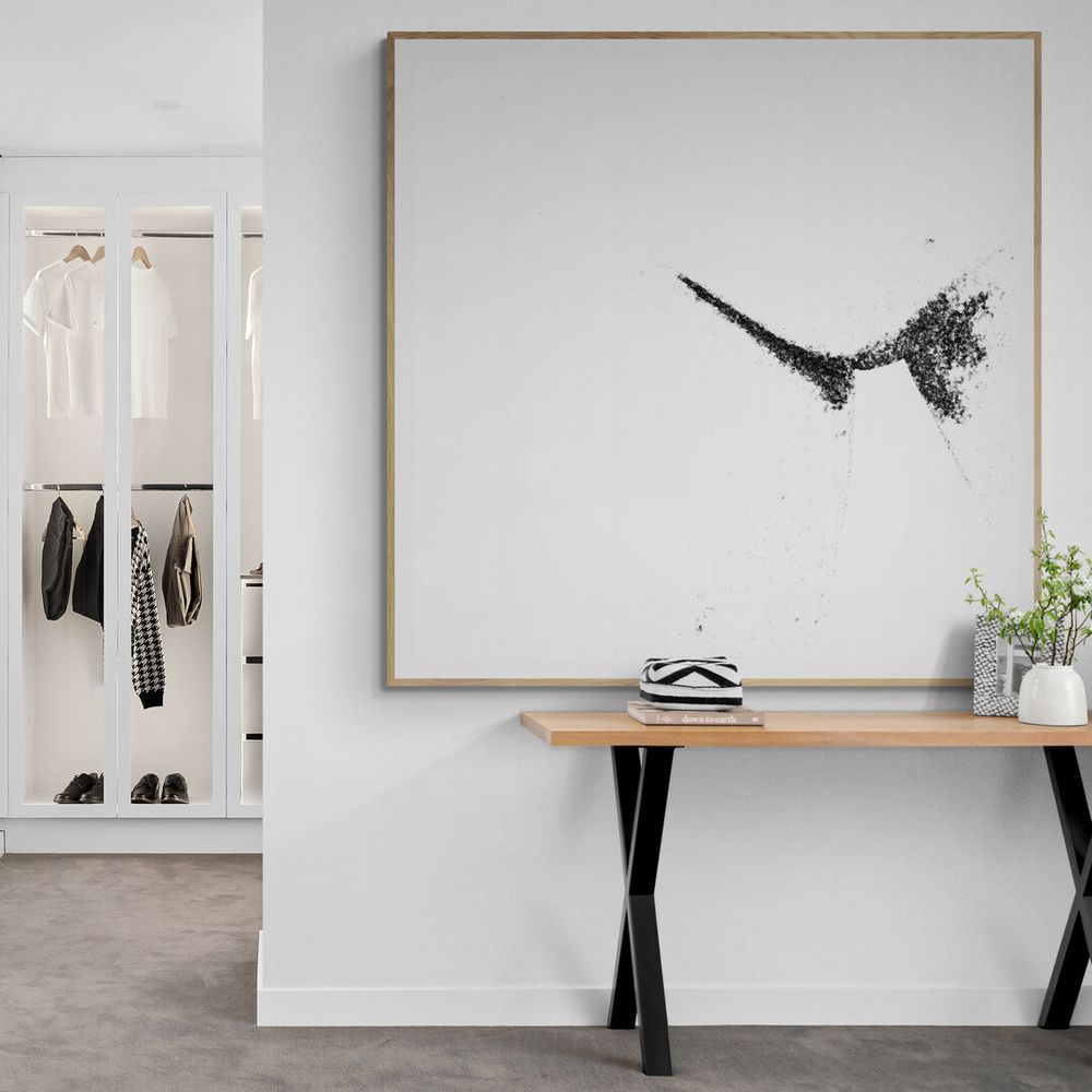 Minimalist entryway with black and white artwork of a bird, wooden console table, and open closet storage space.