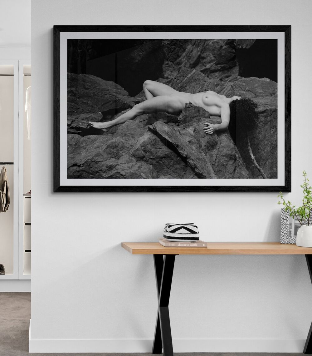 Black and white artistic photograph of a reclining figure on rocky terrain displayed in a modern interior space.