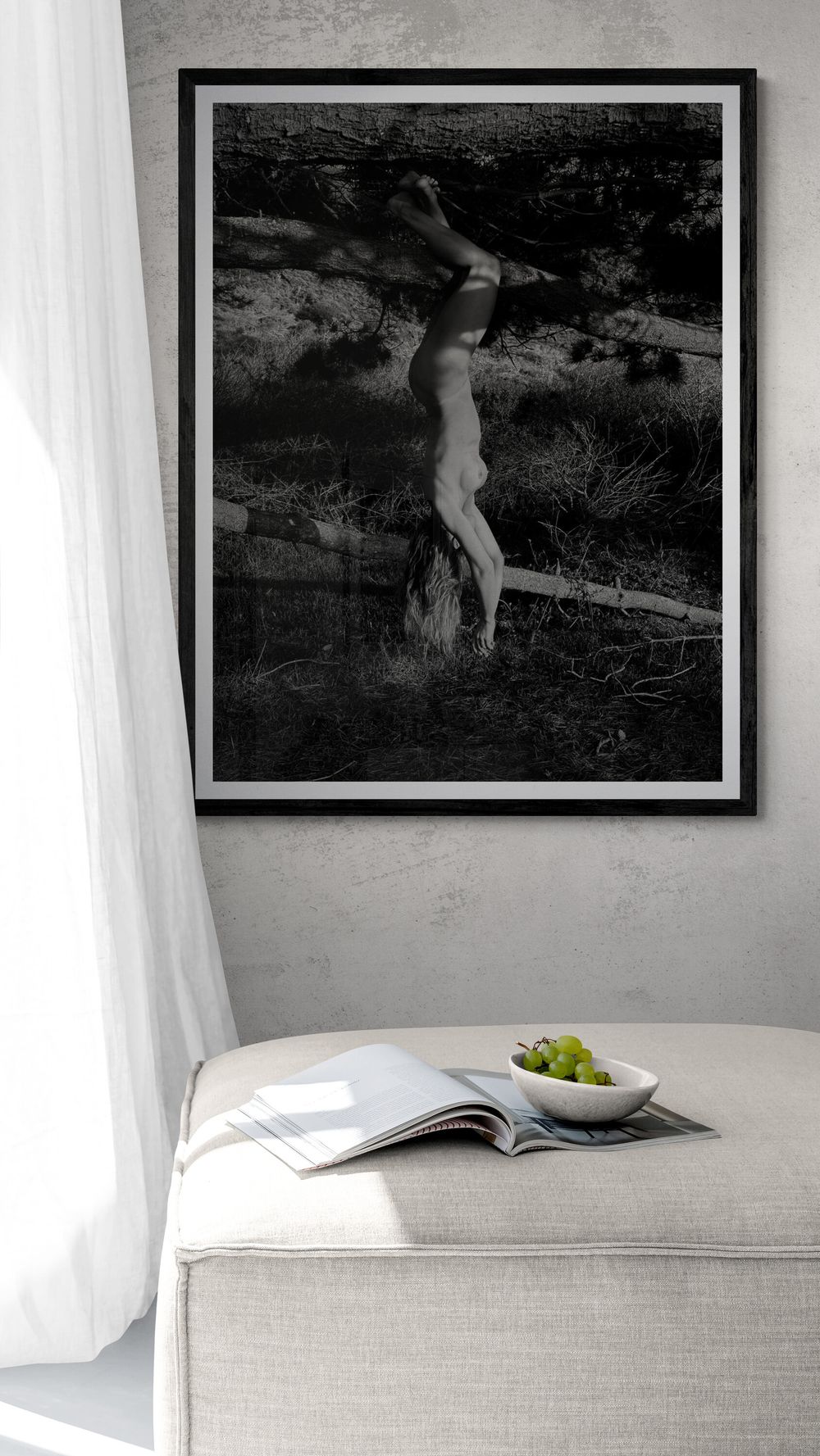 Black and white framed artistic photograph above a light gray couch with an open book and bowl of fruit.