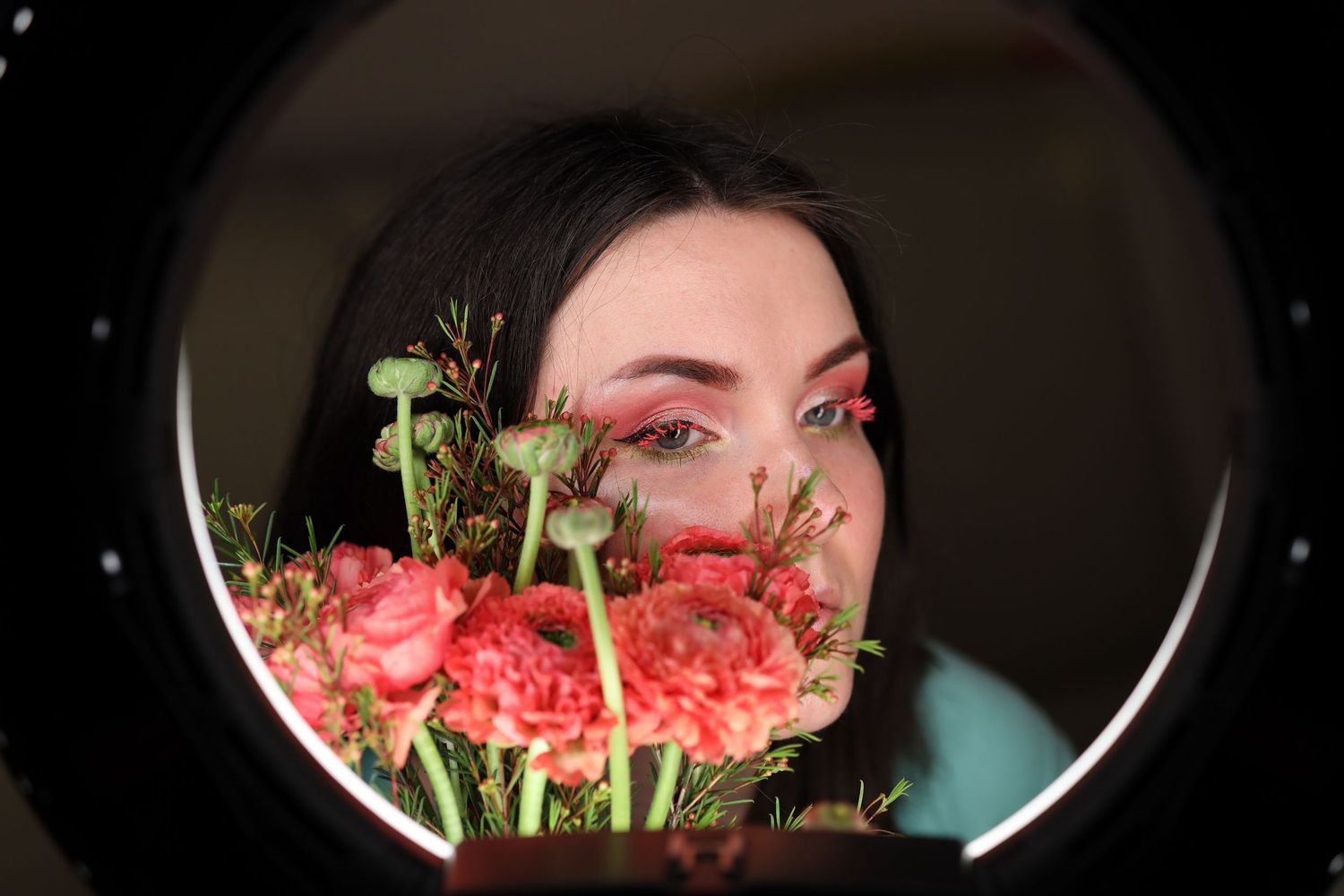 Portrait of a dark-haired girl with bright green-pink makeup and flowers through a ring lamp. Pink eyelashes