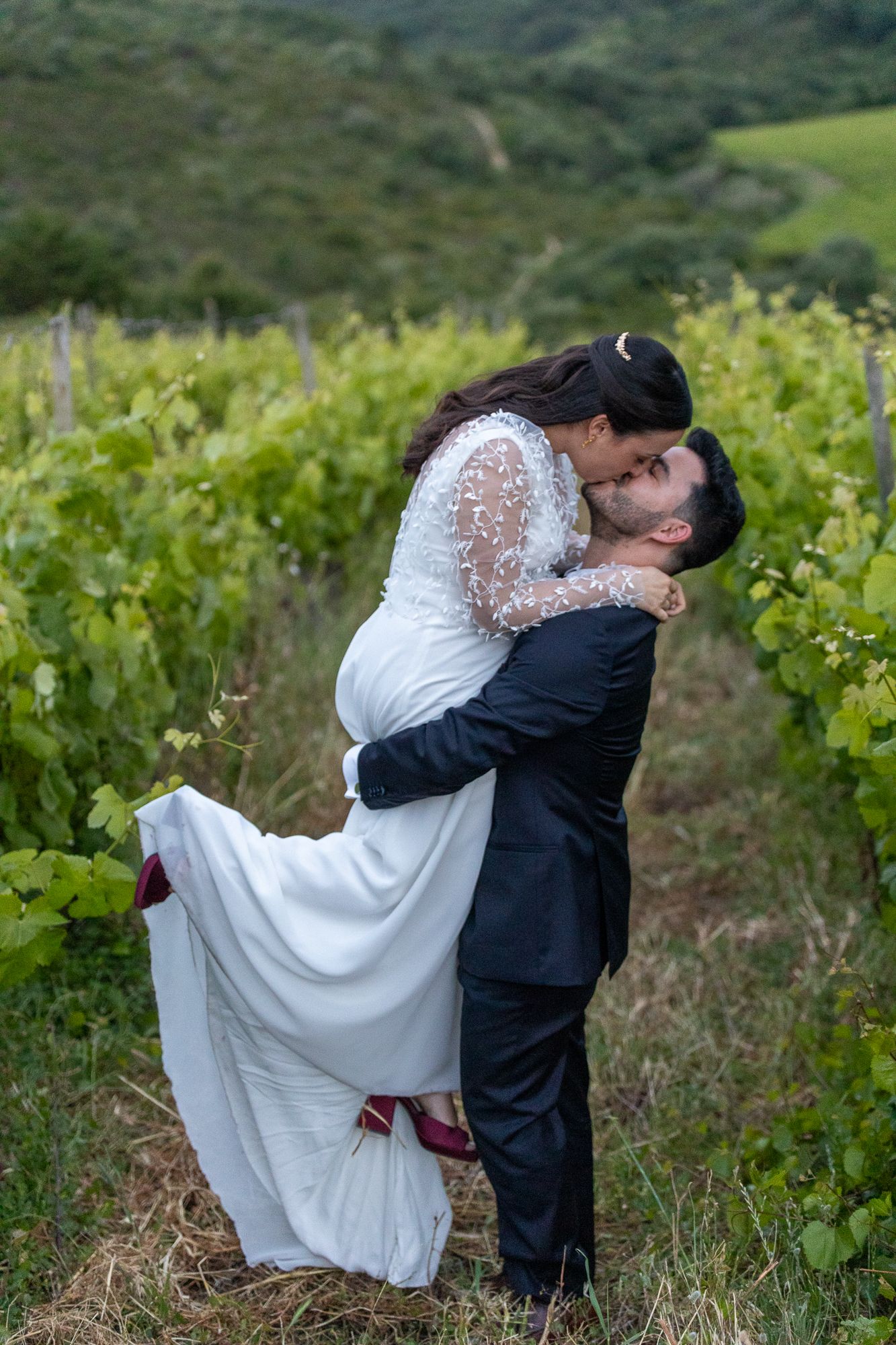 Romantic wedding photos of a couple embracing in a scenic vineyard setting.