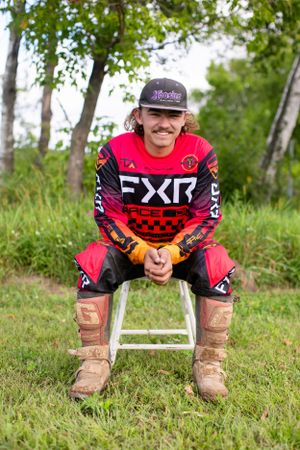 Rider in red FXR motocross gear crouching in grassy outdoor setting.