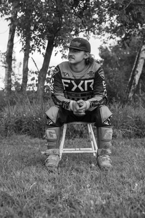 Motocross athlete in FXR gear resting in grassy field.