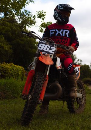 Dirt bike riders in FXR gear lined up on trail with bikes.