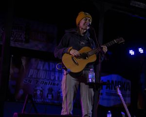 Musicians performing acoustic set on dimly lit stage with blue lighting effects.
