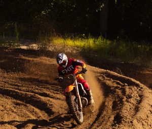 Motocross rider navigates a dirt track through wooded terrain, kicking up dust during an intense race.