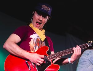 Musicians performing with guitars on stage in dramatic red lighting.
