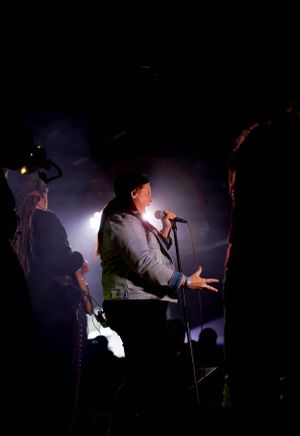 Dark concert venue with performers silhouetted against dramatic backlighting.
