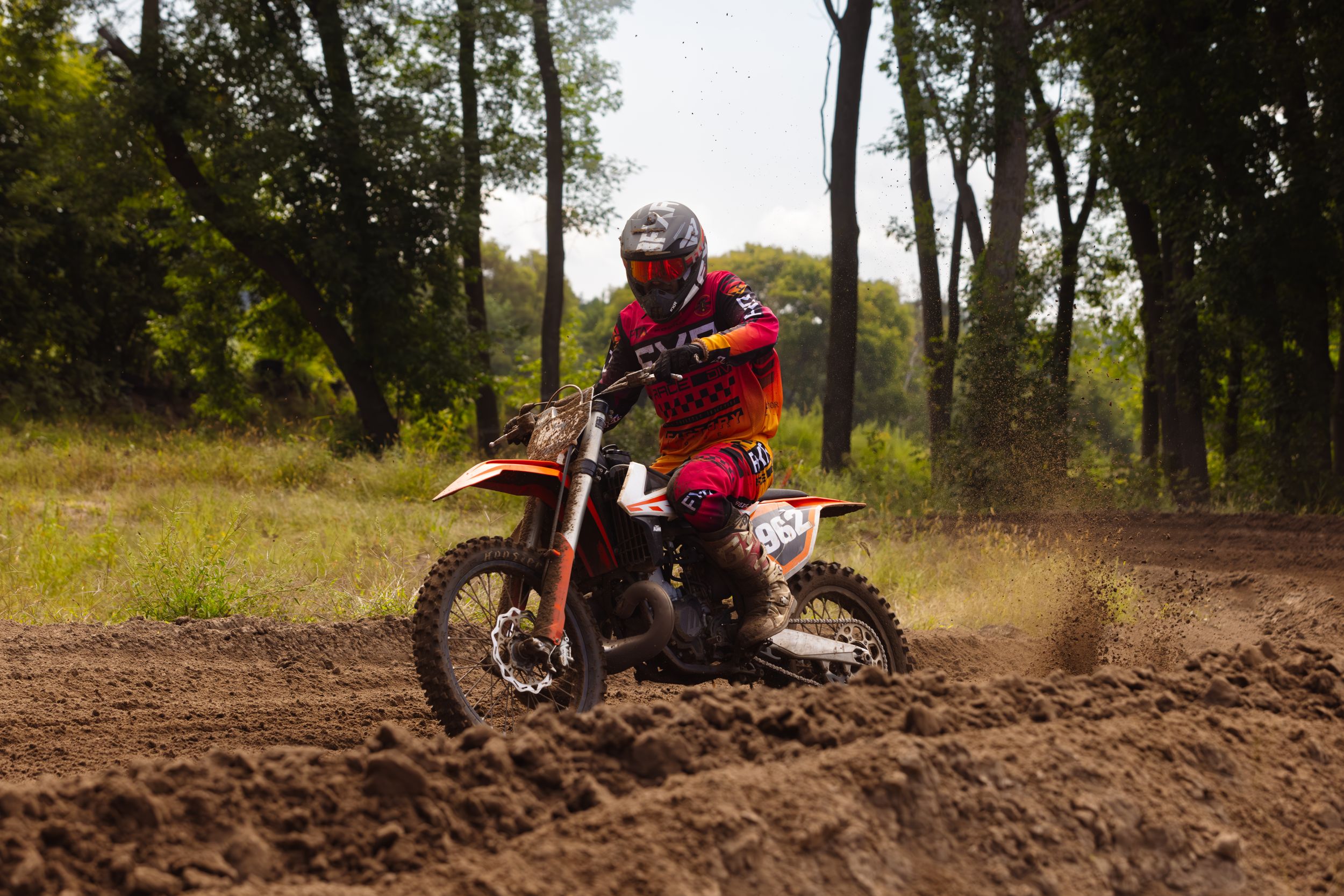 Dirt bike rider takes on challenging wooded motocross track with impressive form.