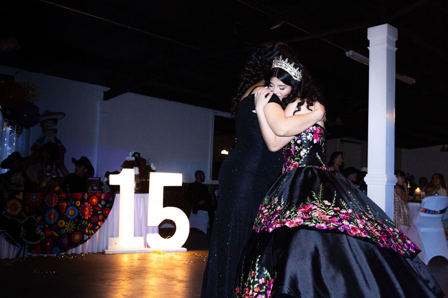 A quinceañera celebration features an ornate black and pink ballgown next to illuminated number 15 display on stage.