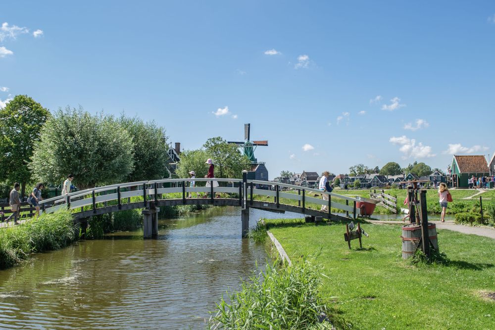 Wooden footbridge with windmill crosses a canal in a traditional Dutch village landscape.