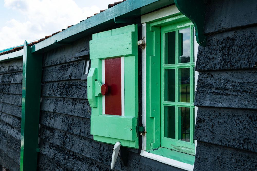 Close-up of a bright green window frame and red door on a dark wooden building in traditional Dutch style.