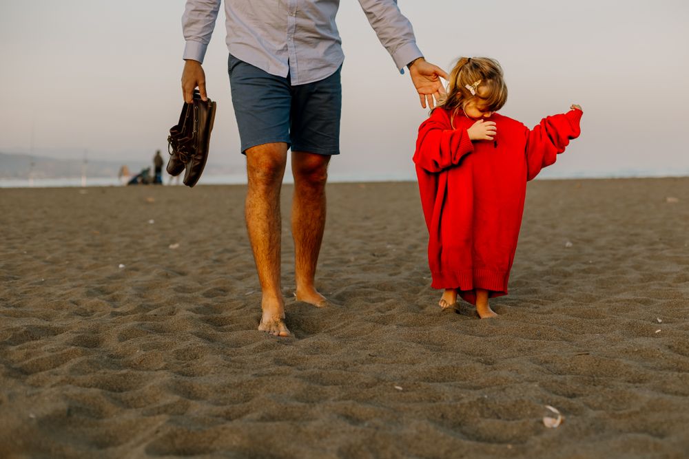Father and his daughter are holding hands, while she happily wears his red sweater.