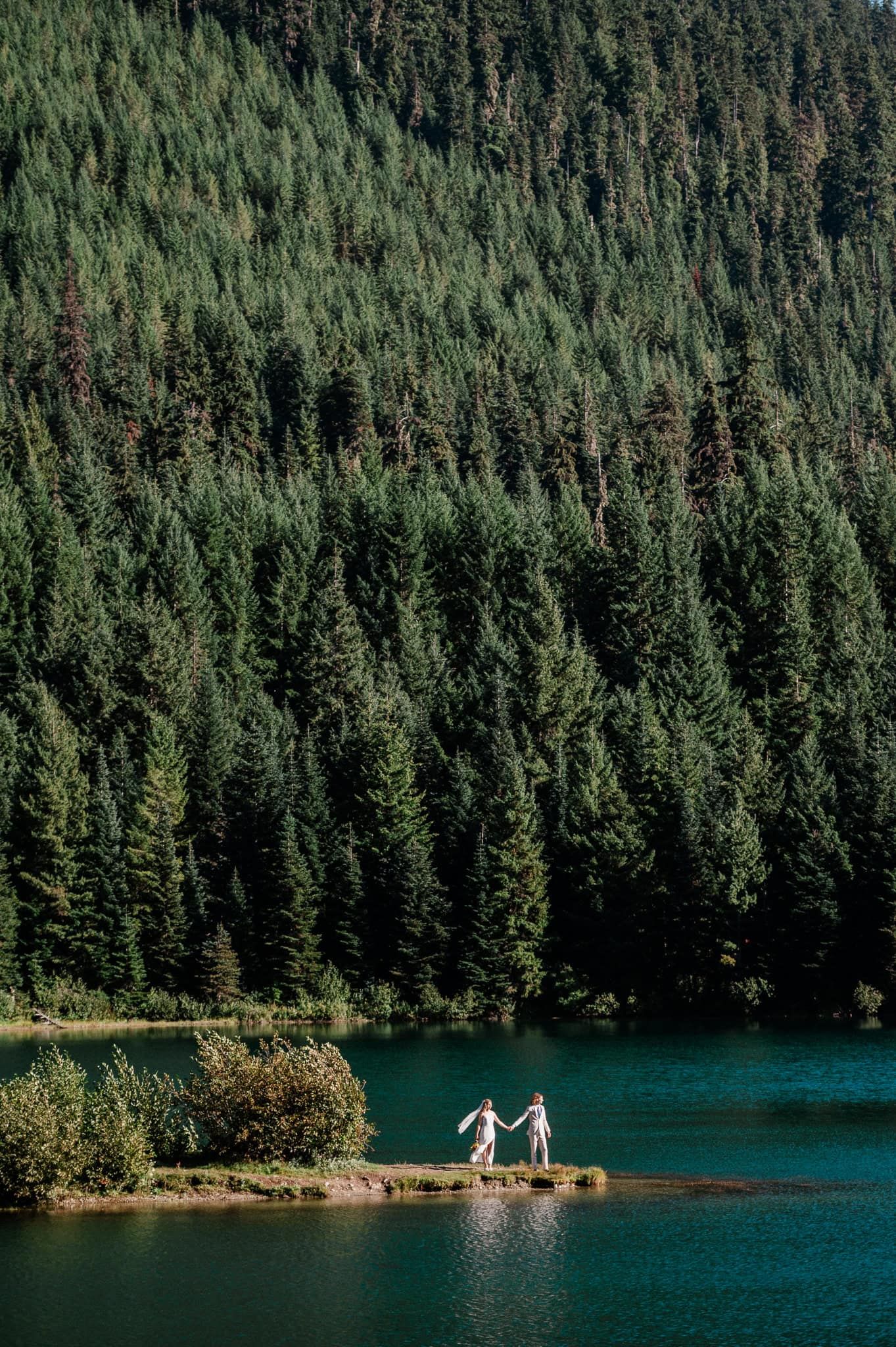 bride and groom in the distance near a blue lake surrounded by mountains