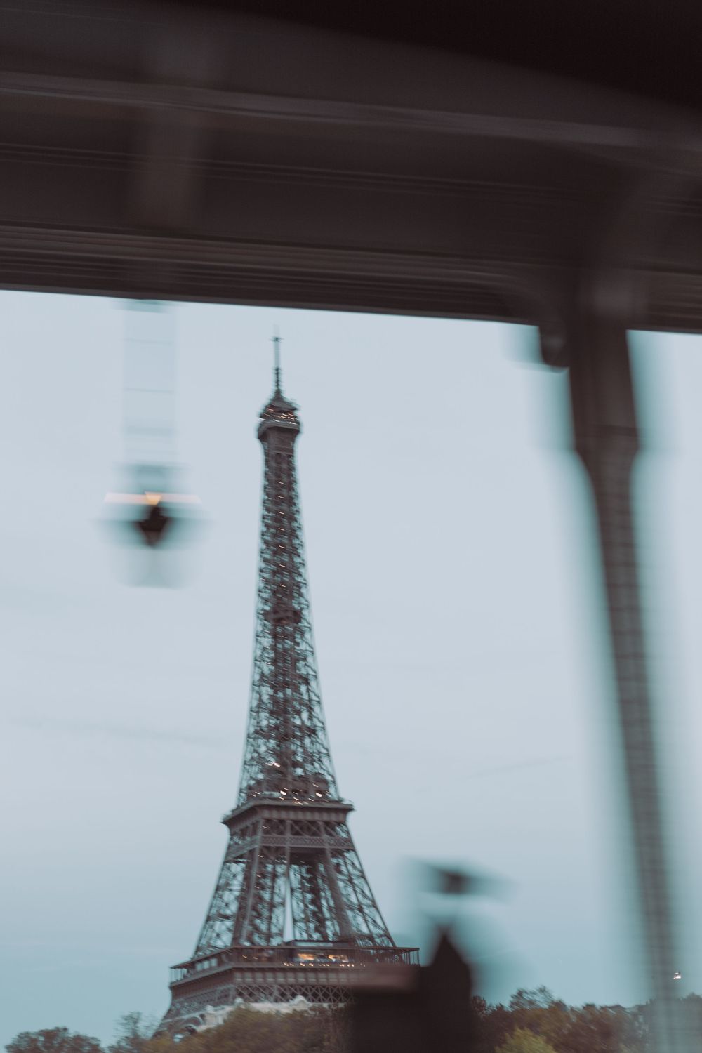 Blurry view of the Eiffel Tower in Paris, France, seen through a vehicle window on a cloudy day.