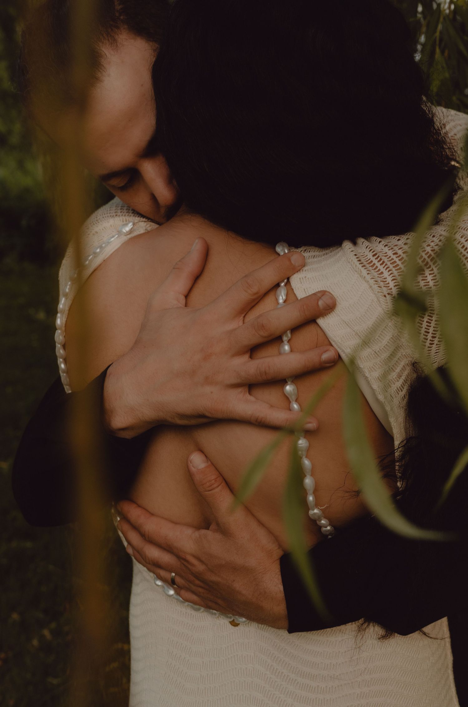 Groom holds bride in his arms tightly under a willow tree.