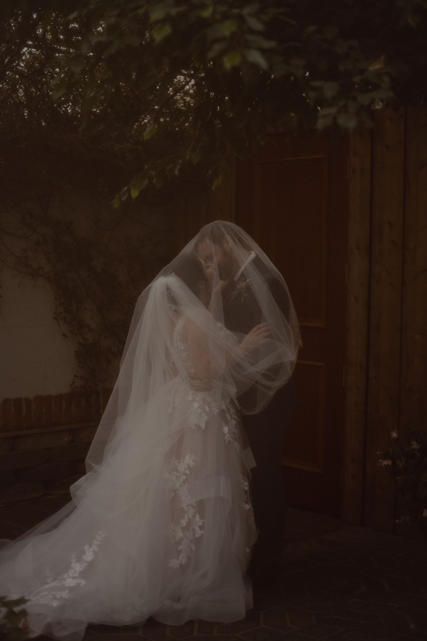 An ethereal shot of the bride and groom draped underneath her veil to share a kiss together. Reception hall is Madison Greenhouse Events.