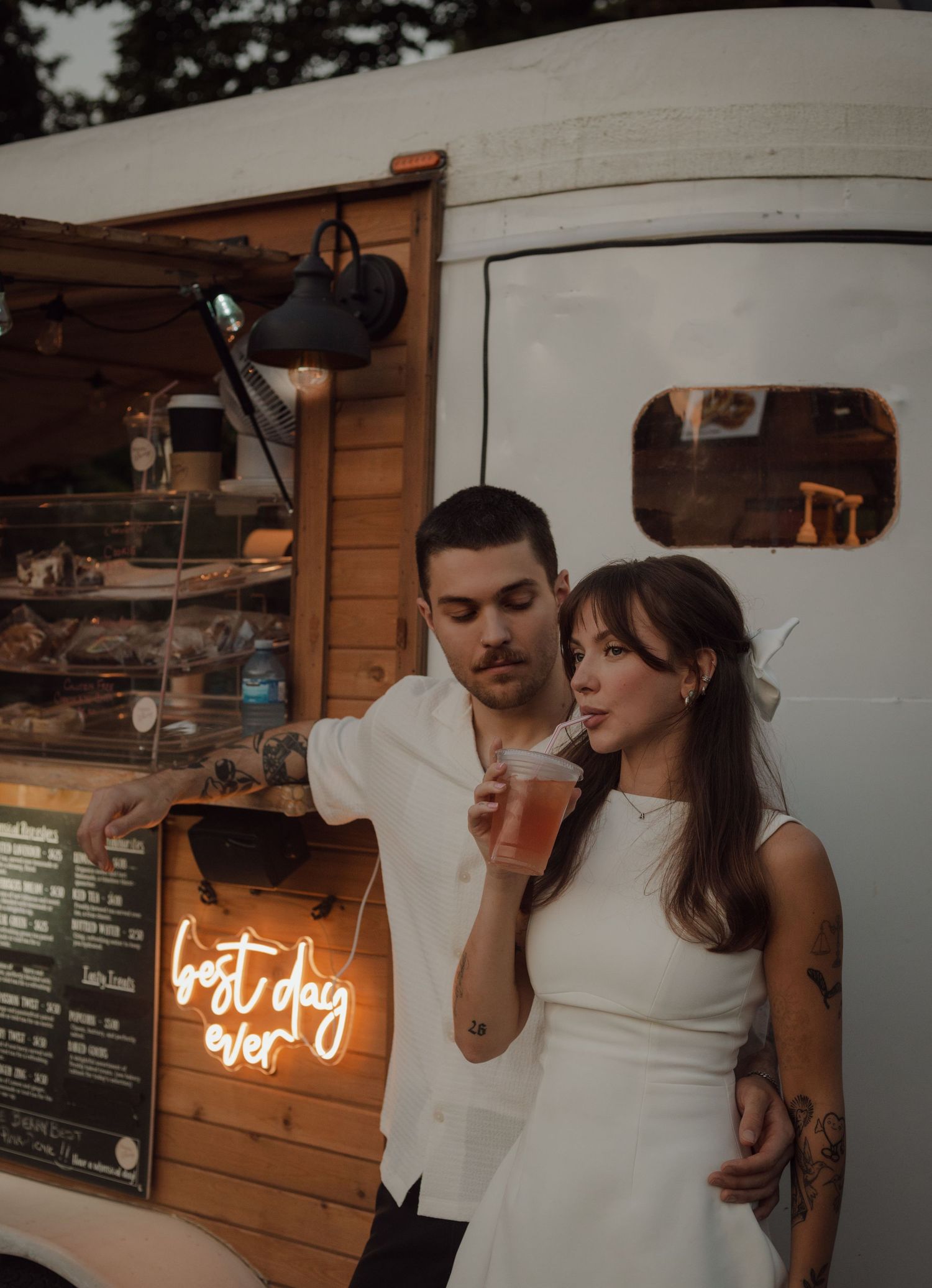 Bride and groom during their elopement standing against a coffee cart. Bride takes a sip of her refreshment.