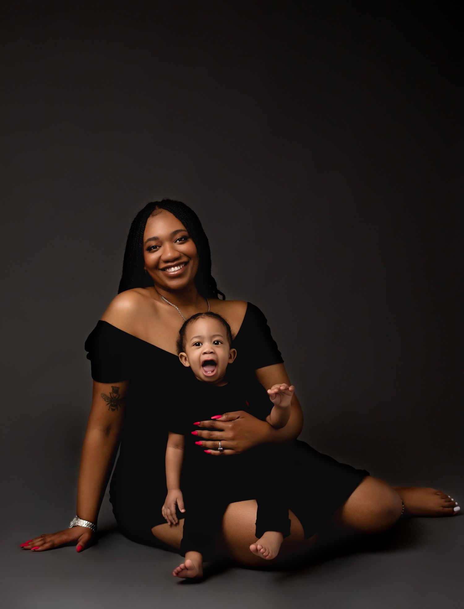 Parent and baby photoshoot in coordinating white shirts against gray background.