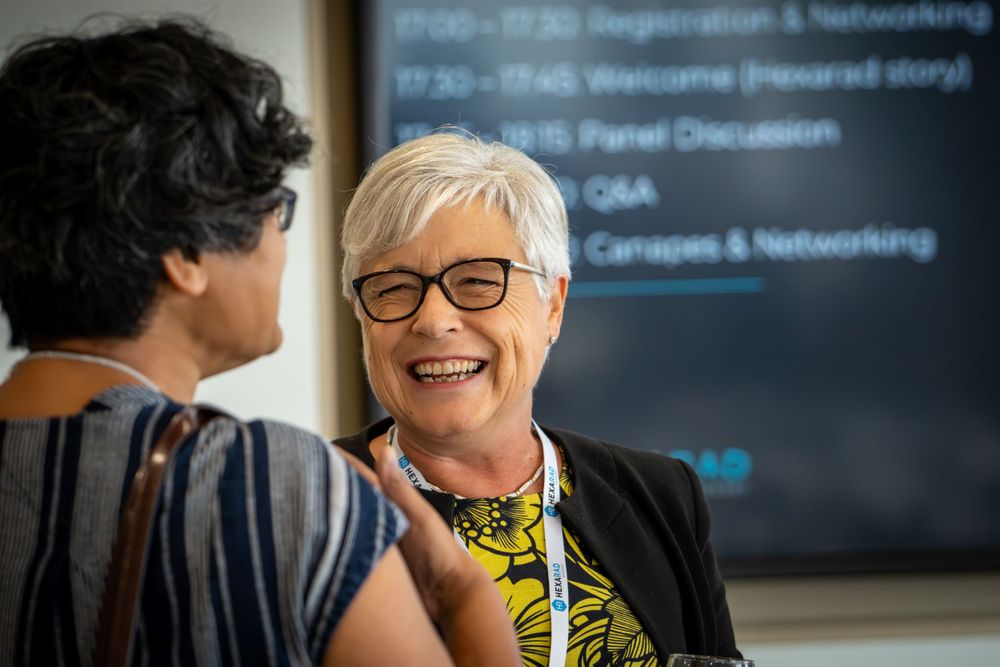 Professional conference or networking event with presentation screen in background.