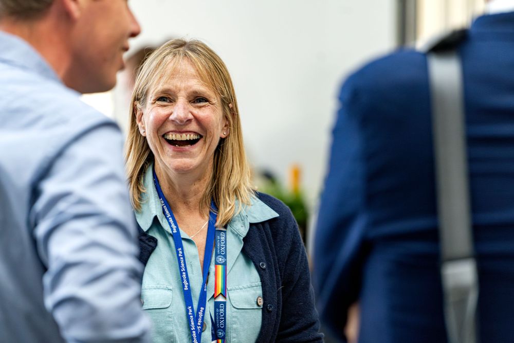 A person with blonde hair smiles joyfully while wearing a staff lanyard during what appears to be a workplace interaction.