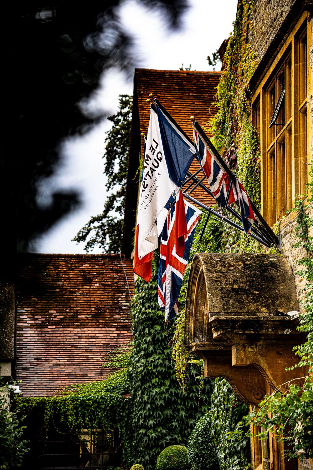 British and French flags displayed on historic stone building with ivy covered walls.