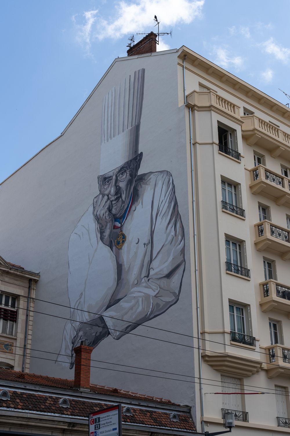 Large artistic mural on white building facade depicting figure in formal attire.