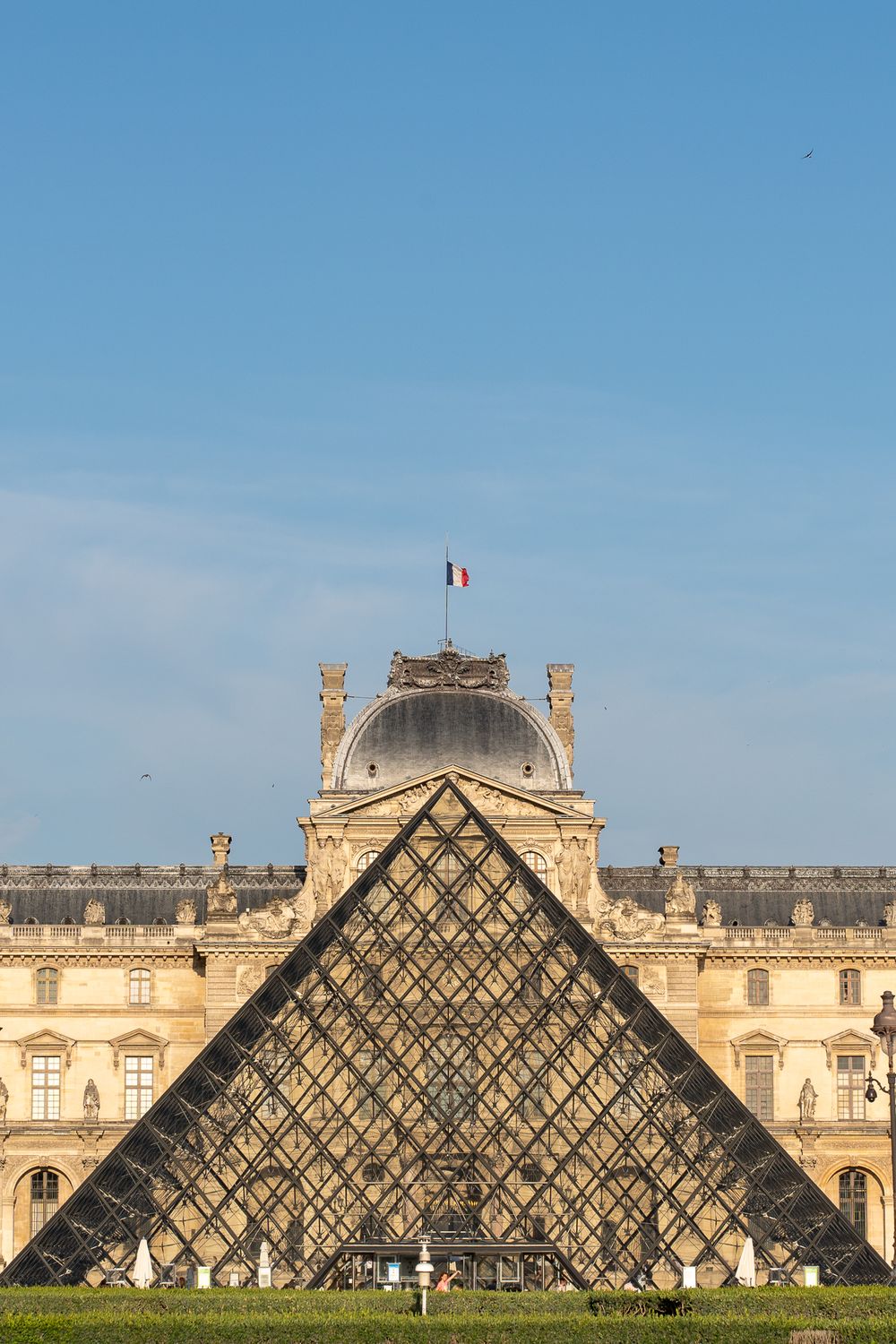 The iconic glass pyramid entrance of the Louvre Museum stands prominently in front of the historic palace facade.