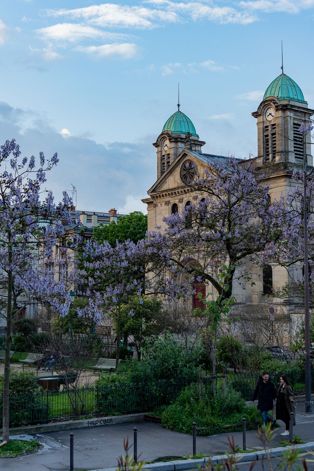 Historic church with twin green domes and flowering trees in spring.