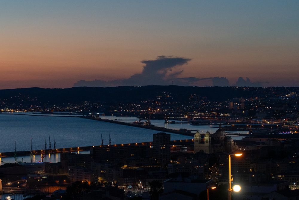 Twilight cityscape with harbor lights and dramatic cloud formation over coastal mountains.